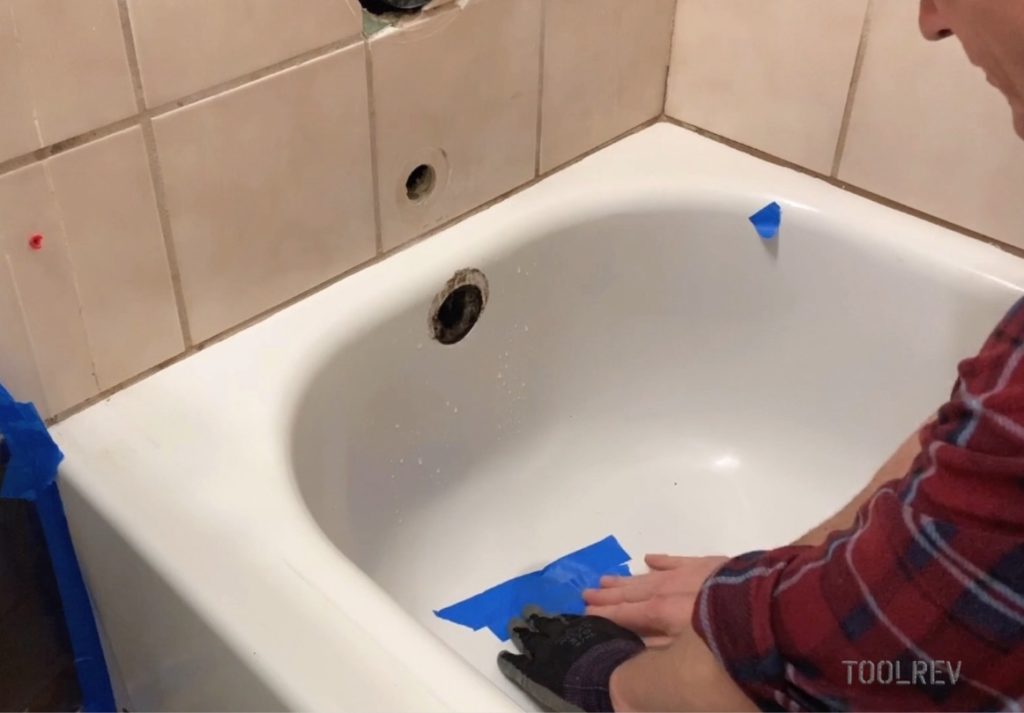 Worker covering bathtub drain with blue tape.