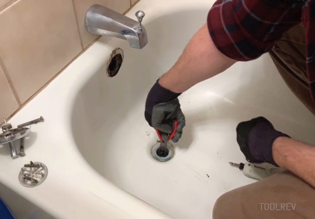 Worker using pliers to unscrew bathtub drain flange.