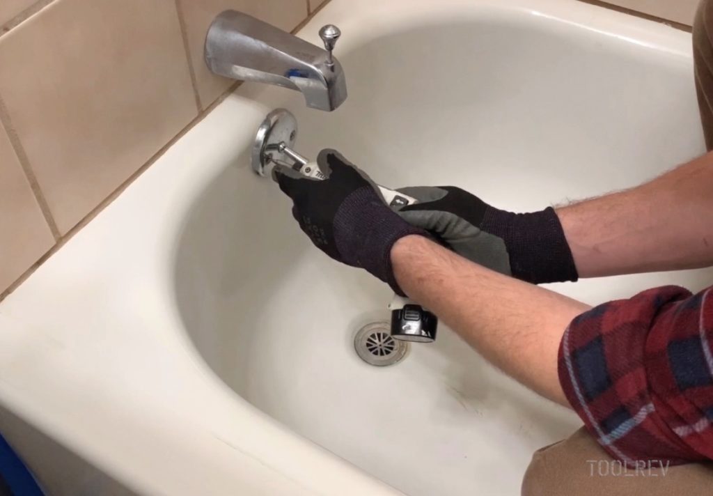 Worker unscrewing bathtub overflow cover.