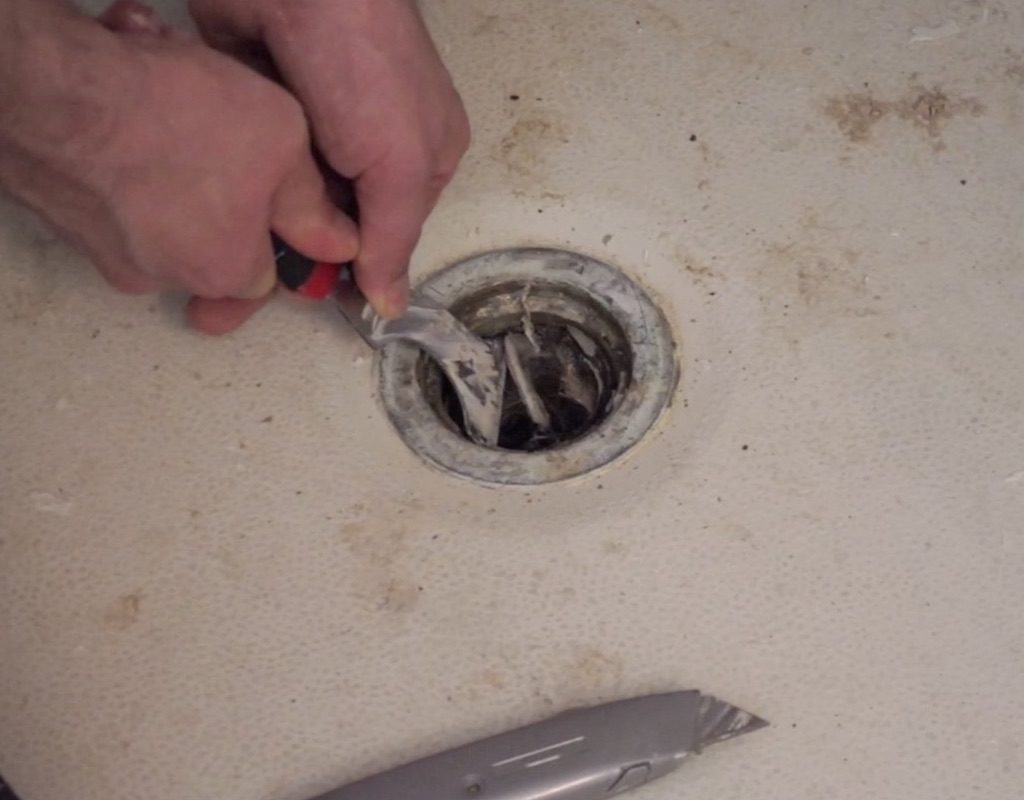 worker using a tool to remove caulking from shower drain