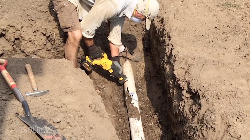 Worker cutting drain line with a reciprocating saw