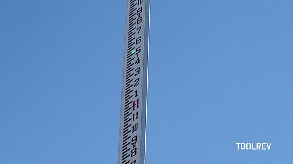 Green laser spot shining on a gray grade rod pole against a blue sky background.
