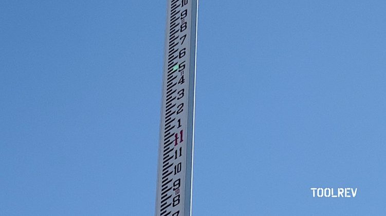 Green laser spot shining on a gray grade rod pole against a blue sky background.