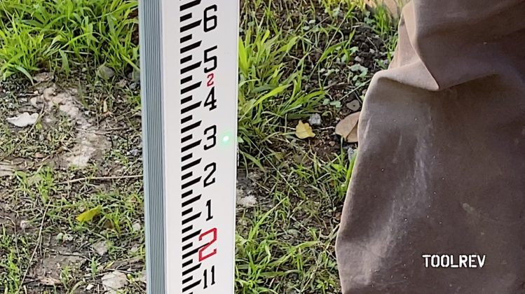 Green laser spot shown on a gray colored grade rod outdoors.