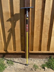 Task support rod in yellow coloring leaning against a fence.