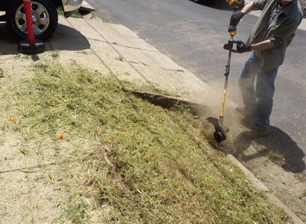 DeWalt FlexVolt string trimmer edging along a sidewalk DeWalt FlexVolt string trimmer edging along a sidewalk