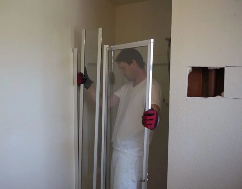 Man carefully removing a shower door during bathroom renovation