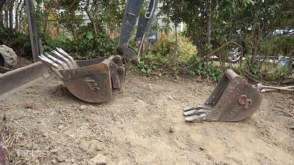 Two mini excavator buckets, one mounted and one on the ground