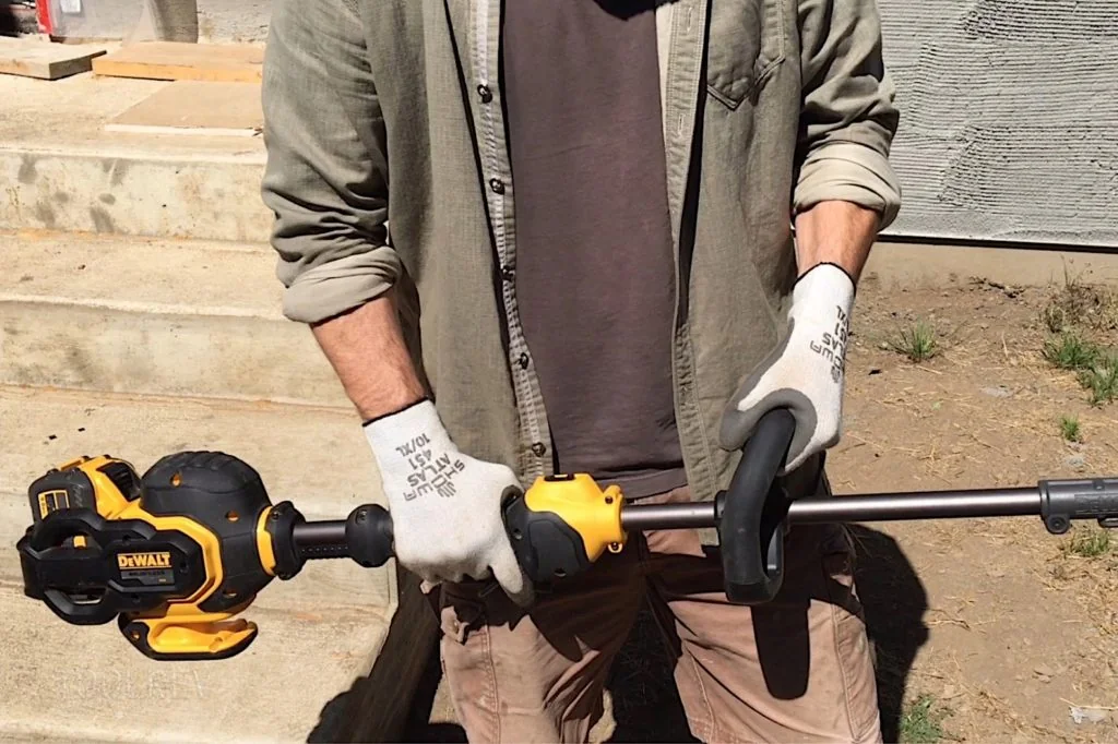 Hands on a DeWalt FlexVolt string trimmer handle Hands holding the shaft and auxiliary handle of a DeWalt FlexVolt string trimmer