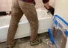 How To Remove a Bathtub Worker lifting an old bathtub up from the bathroom floor during removal