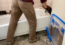 How To Remove a Bathtub Worker lifting an old bathtub up from the bathroom floor during removal