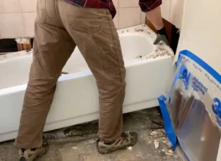 How To Remove a Bathtub Worker lifting an old bathtub up from the bathroom floor during removal