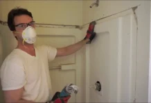 Worker in a dust mask removing a shower surround wall