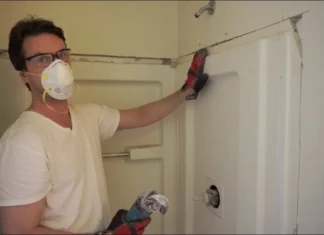 Worker in a dust mask removing a shower surround wall