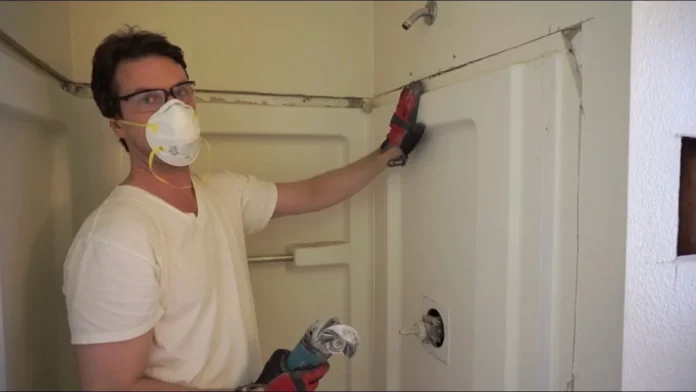 Worker in a dust mask removing a shower surround wall